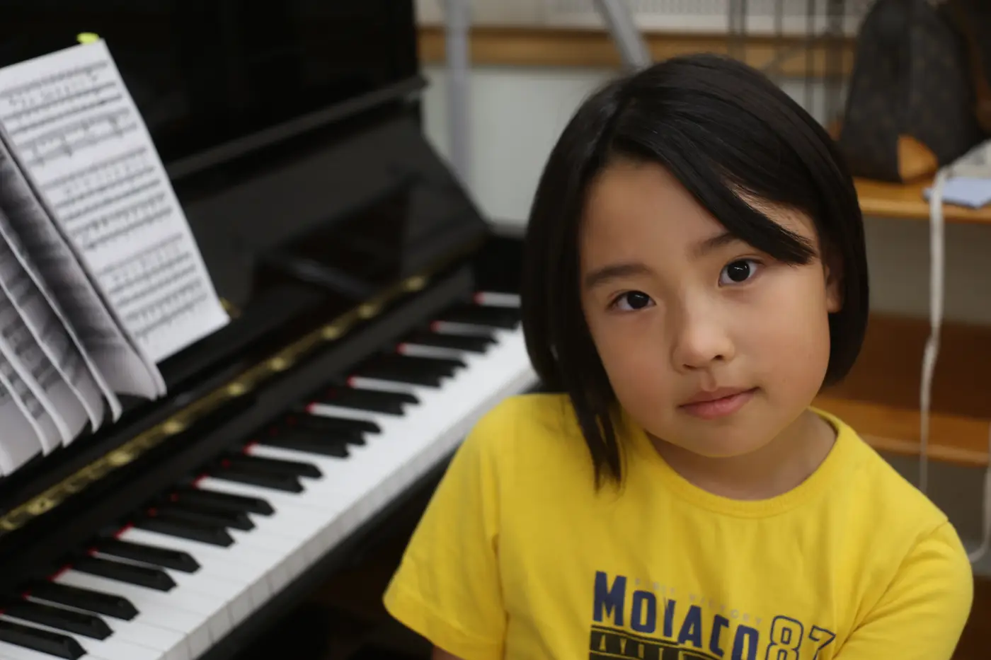 ピアノの前でこちらを見る子役